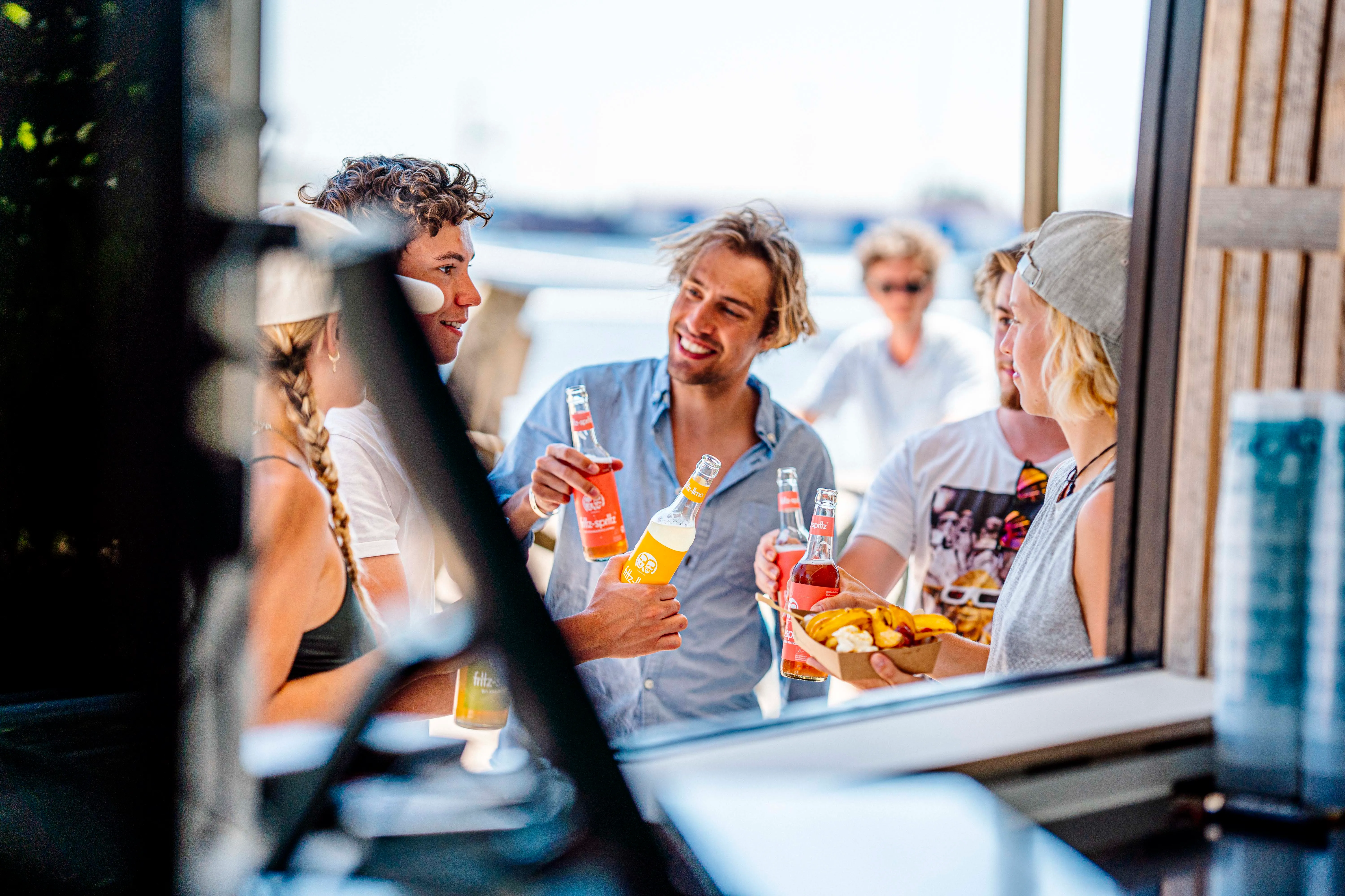 Freunde lachen mit Drinks und Snacks an der Supieria Beachbar